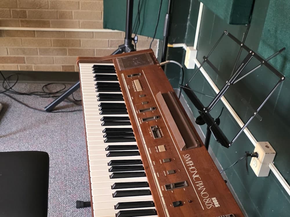 A Korg Symphonic Piano 80S on its stand, with a microphone and a folding music stand set up beside it.